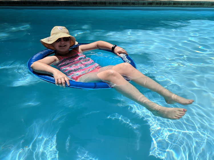 A young girl wearing a sunhat and sunglasses floating in a pool