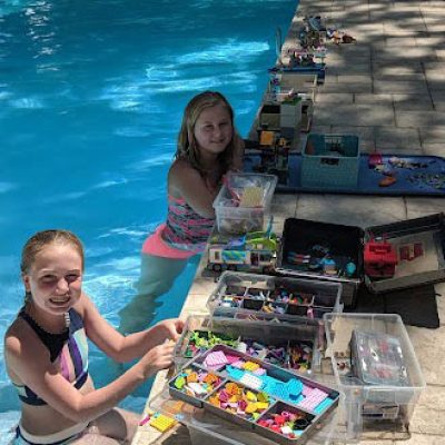 Two young girls sitting by the edge of the pool, playing with Legos