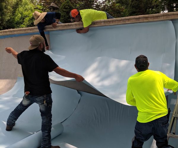 Workers installing a piece of PVC pool liner.